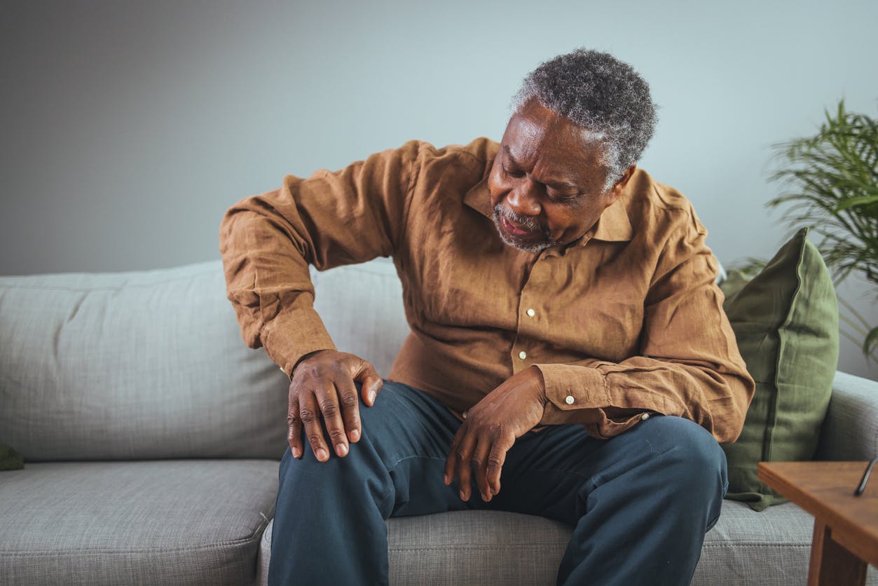 Senior black man standing up and experiencing knee pain stock image