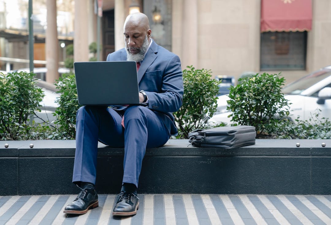 senior gentleman wearing a suit working on his laptop outside of his office stock photo
