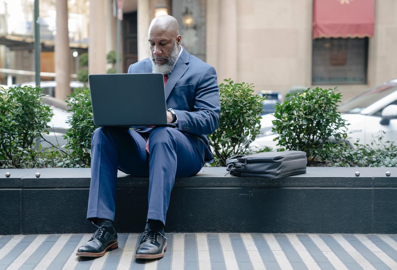 senior gentleman wearing a suit working on his laptop outside of his office stock photo