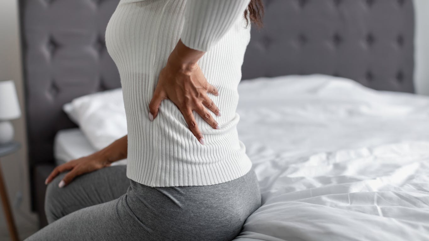 Close up of a woman sitting on a bed experiencing back pain