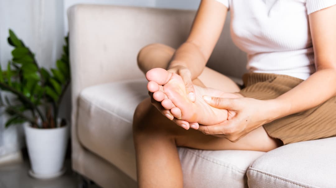 woman sitting on sofa feeling pain in her foot at home stock photo