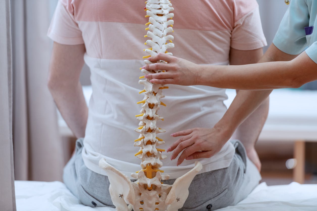 Caucasian nurse holding spine model against the patients backs. Clinic interior. stock photo