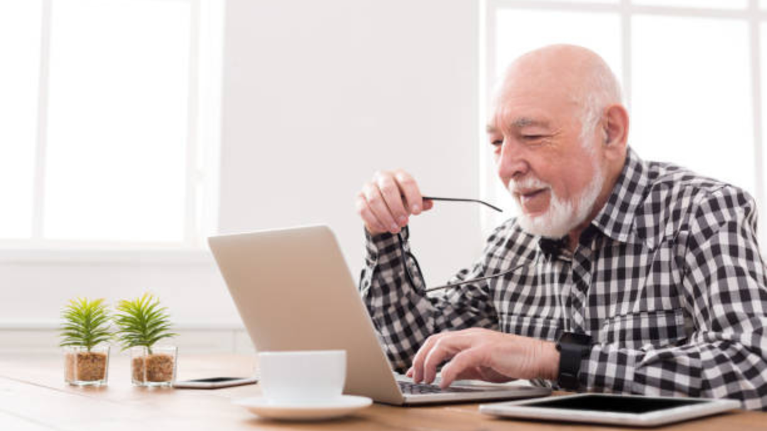 senior man with his glasses in his hand working in front of his laptop stock photo