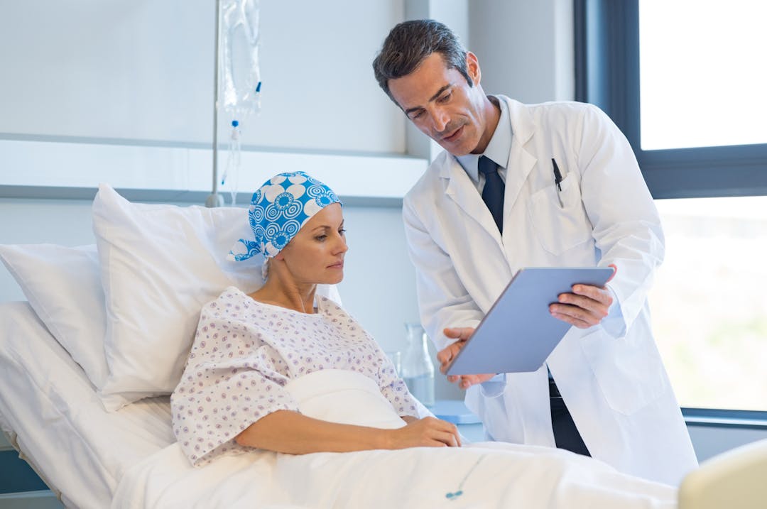 woman in a hospital wearing a bandana being shown information by her doctor stock photo