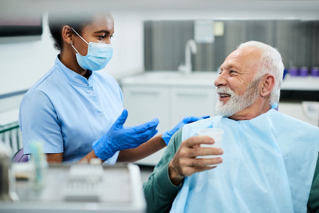 Happy senior man and dentist assistant talking during appointment at dental clinic. stock photo